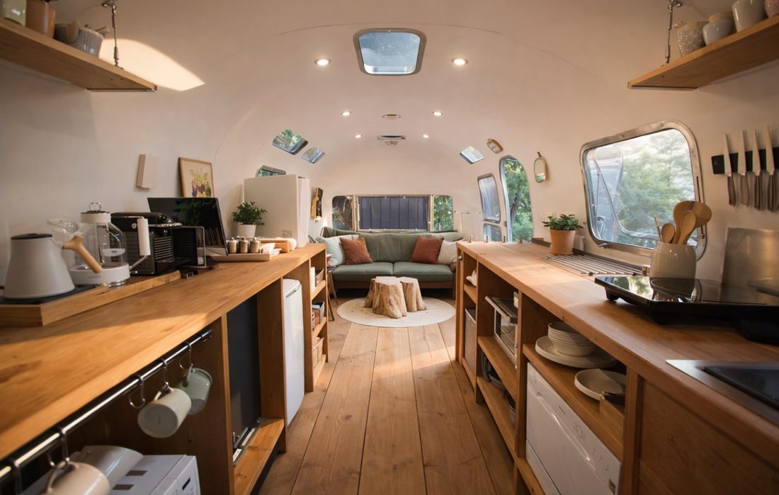 Concept rendering: the interior of an Airstream with a timber kitchen, sofa and forest views